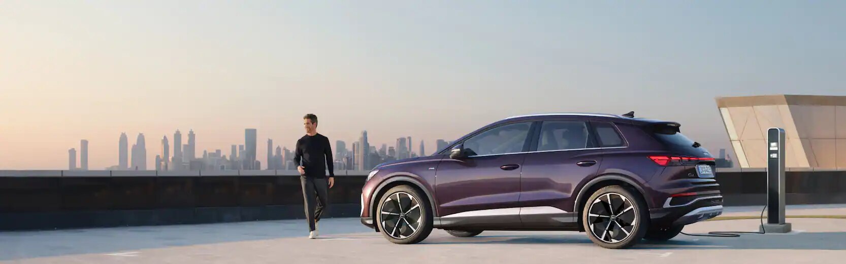 Man walking near Audi Q4 e-tron which is plugged in and charging. 