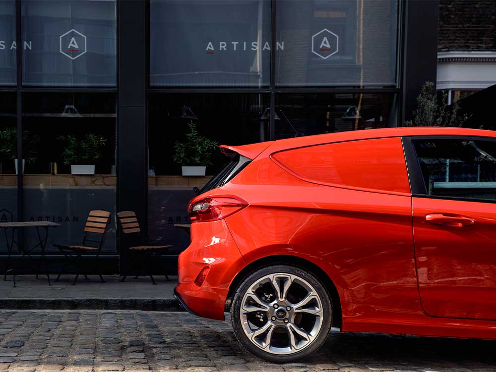 Used Ford Fiesta van Image Card featuring a red second hand ford fiesta rear half of the vehicle shot including the drivers side door and drivers side rear wheel. Side on photograph.