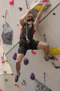 Male climber, mid climb holding onto a large boulder at the Lookers National Universities Lead and Speed Climbing Championships.