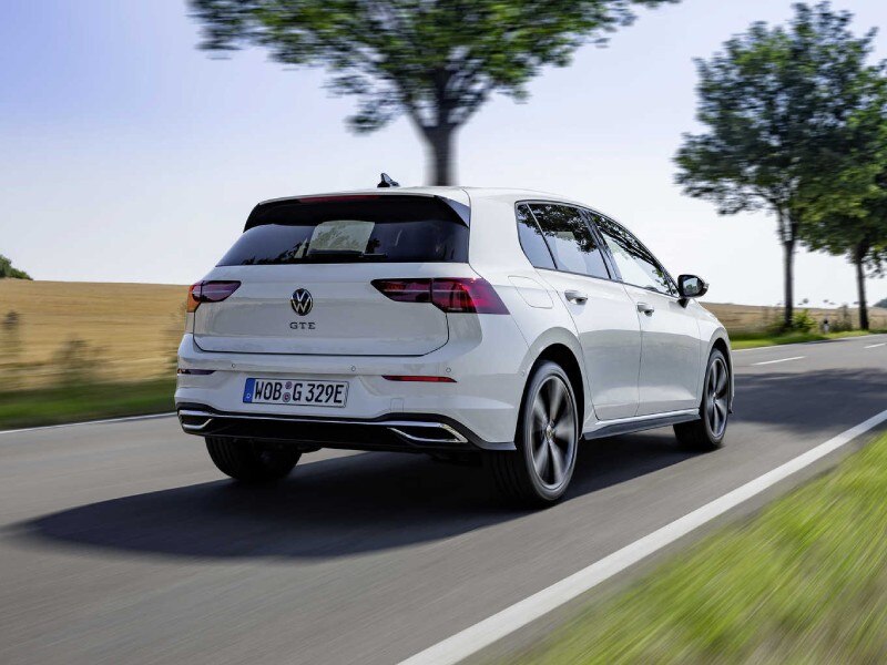Plug-in Hybrid Electric Vehicle PHEVs image card featuring the backend of a Plug-in Hybrid Volkswagen Golf e in white driving on a country road.