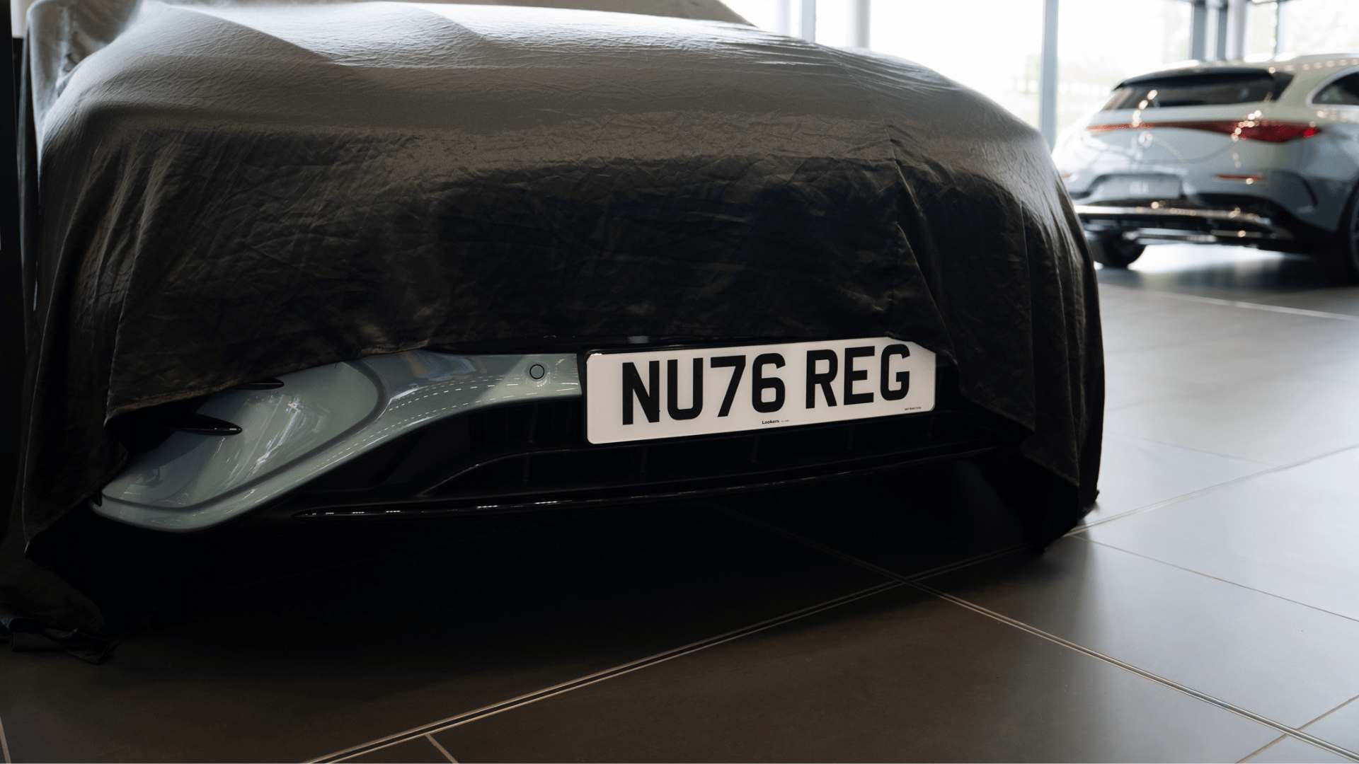 Luxury new car with cover over it being unveiled to show a 76-registration plate