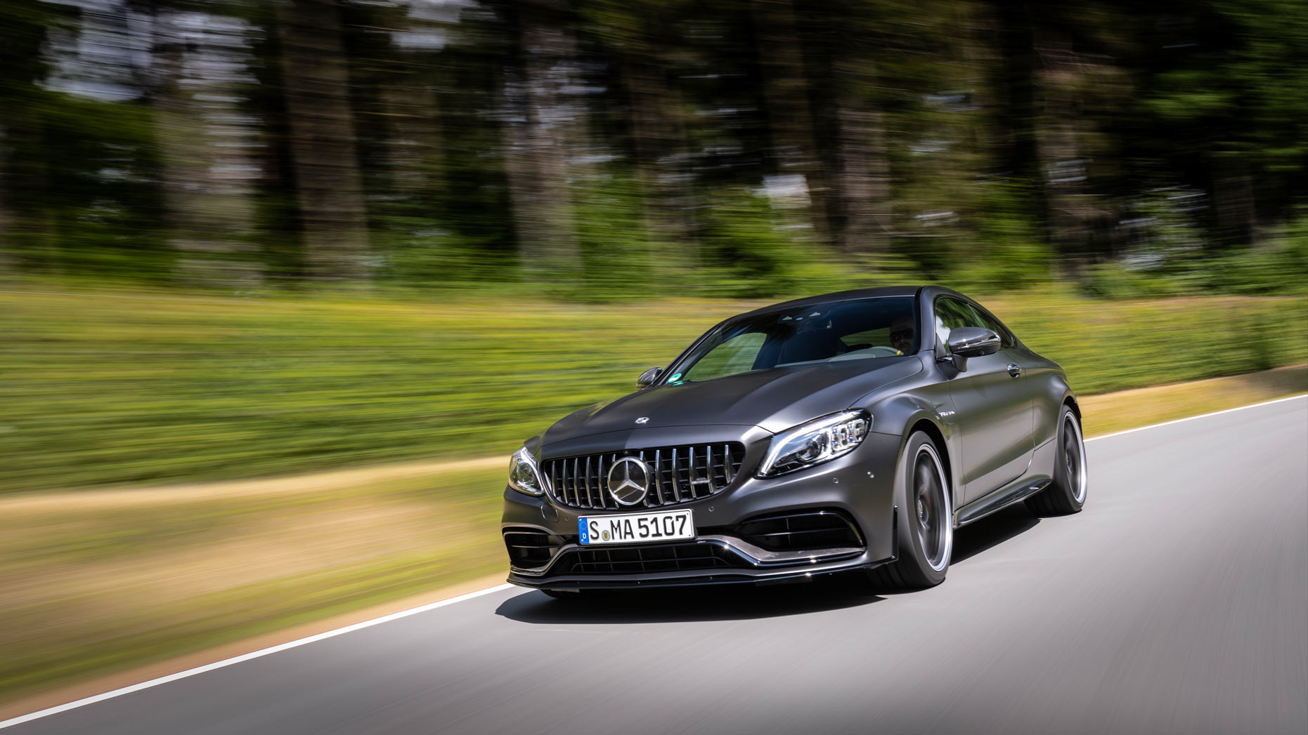 A grey Mercedes-AMG C 63 Coupe travelling along a woodland route