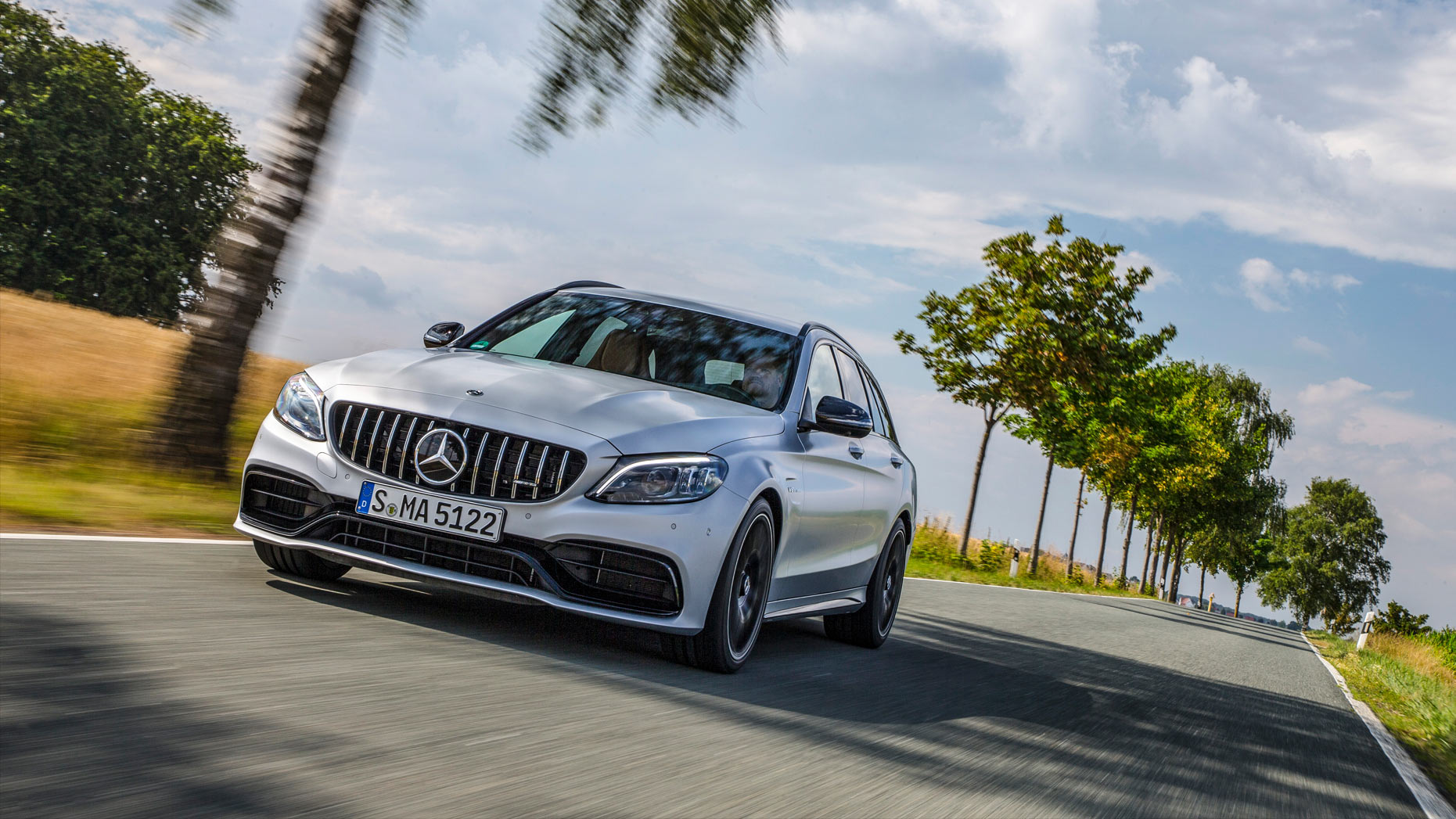 A silver Mercedes-AMG C 63 Estate moving down a tree-lined road