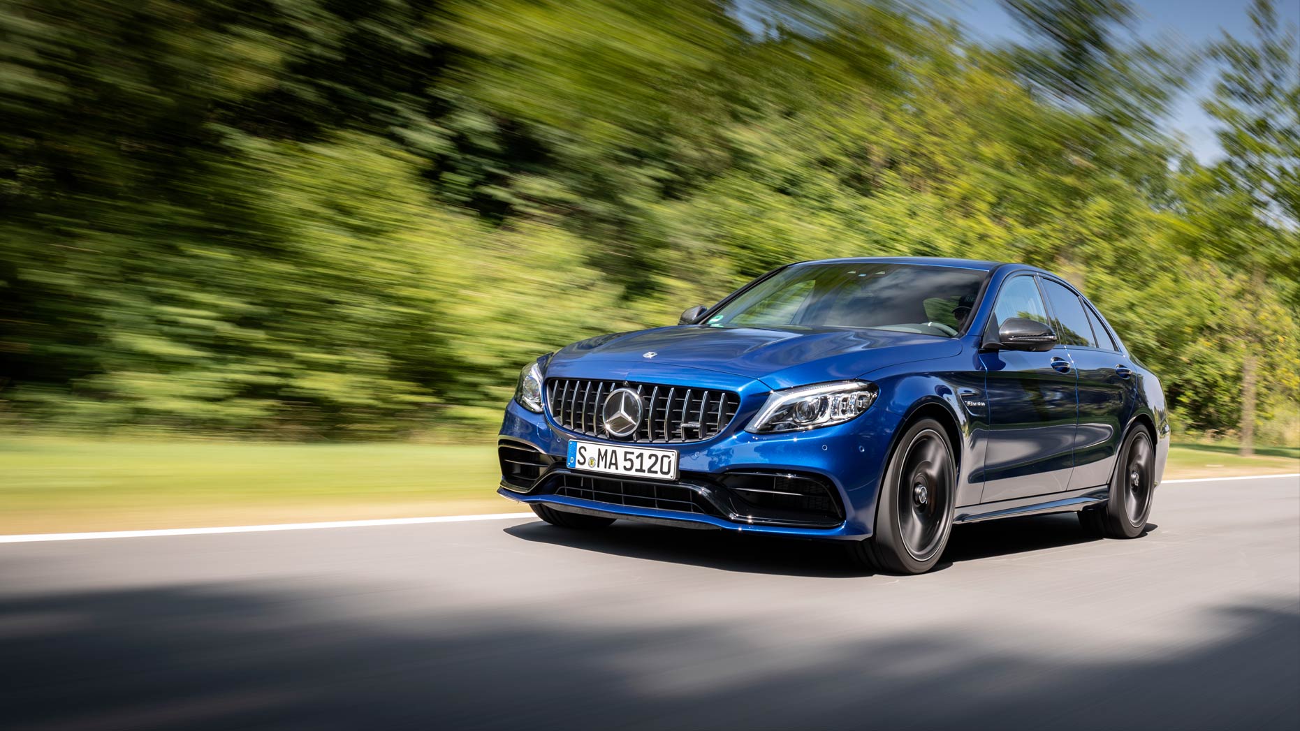 A blue Mercedes-AMG C 63 Saloon travelling along a tree-lined route