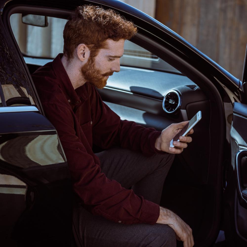 Man in parked Mercedes-Benz looking at phone