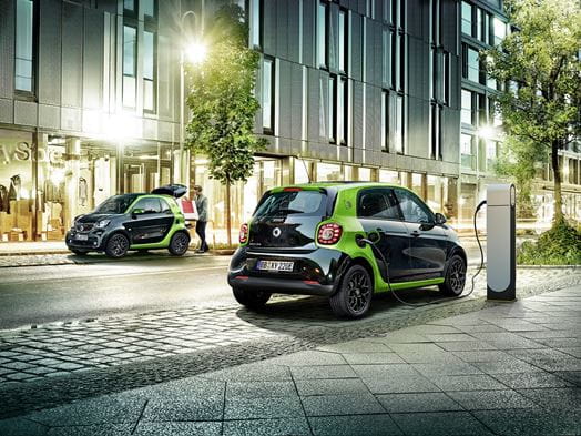 Cheapest Electric Cars on the market Lookers Blog Image featuring the all electric smart EQ, one of the most affordable electric cars front shot and rear shot of the vehicle parked on a commercial street charging on a public electric car charger.
